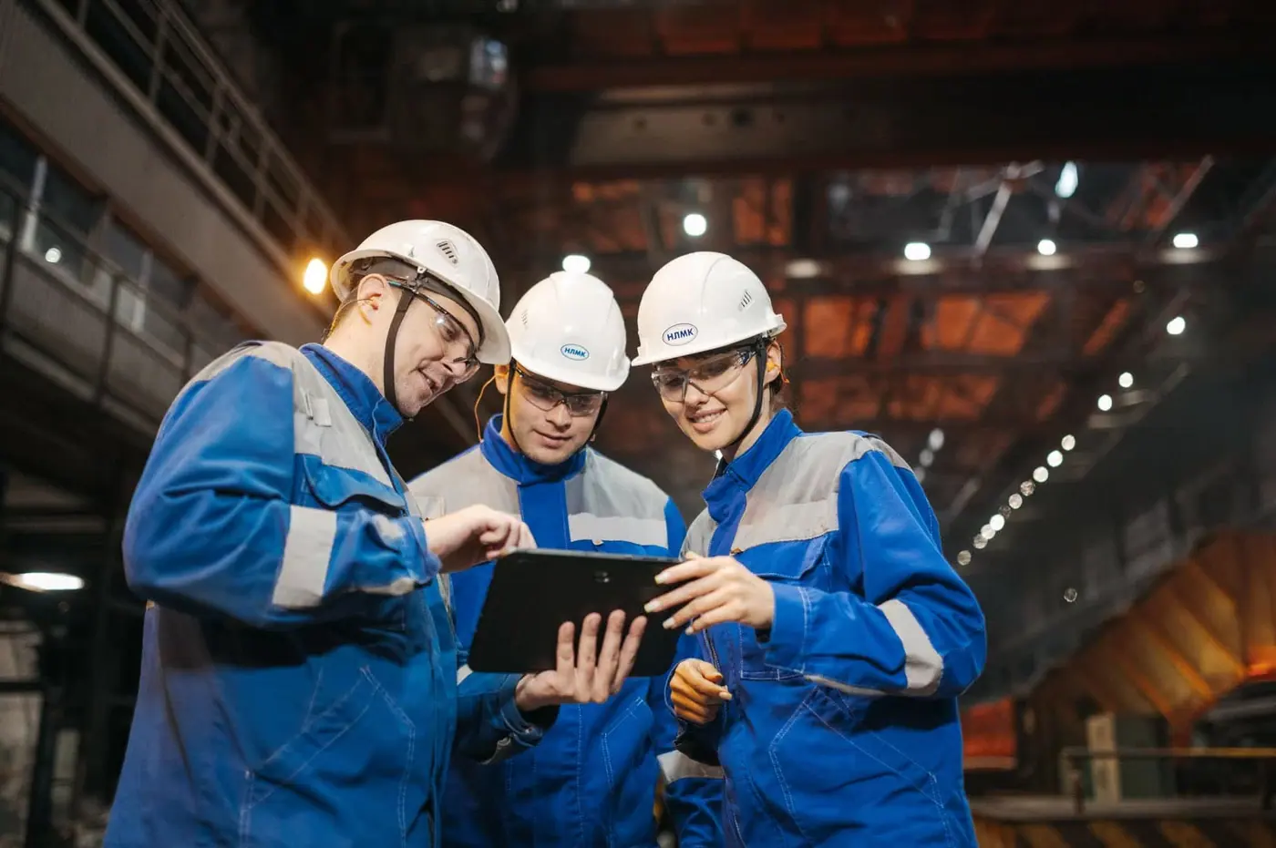 Trois techniciens HSE consultant une tablette dans un atelier industriel