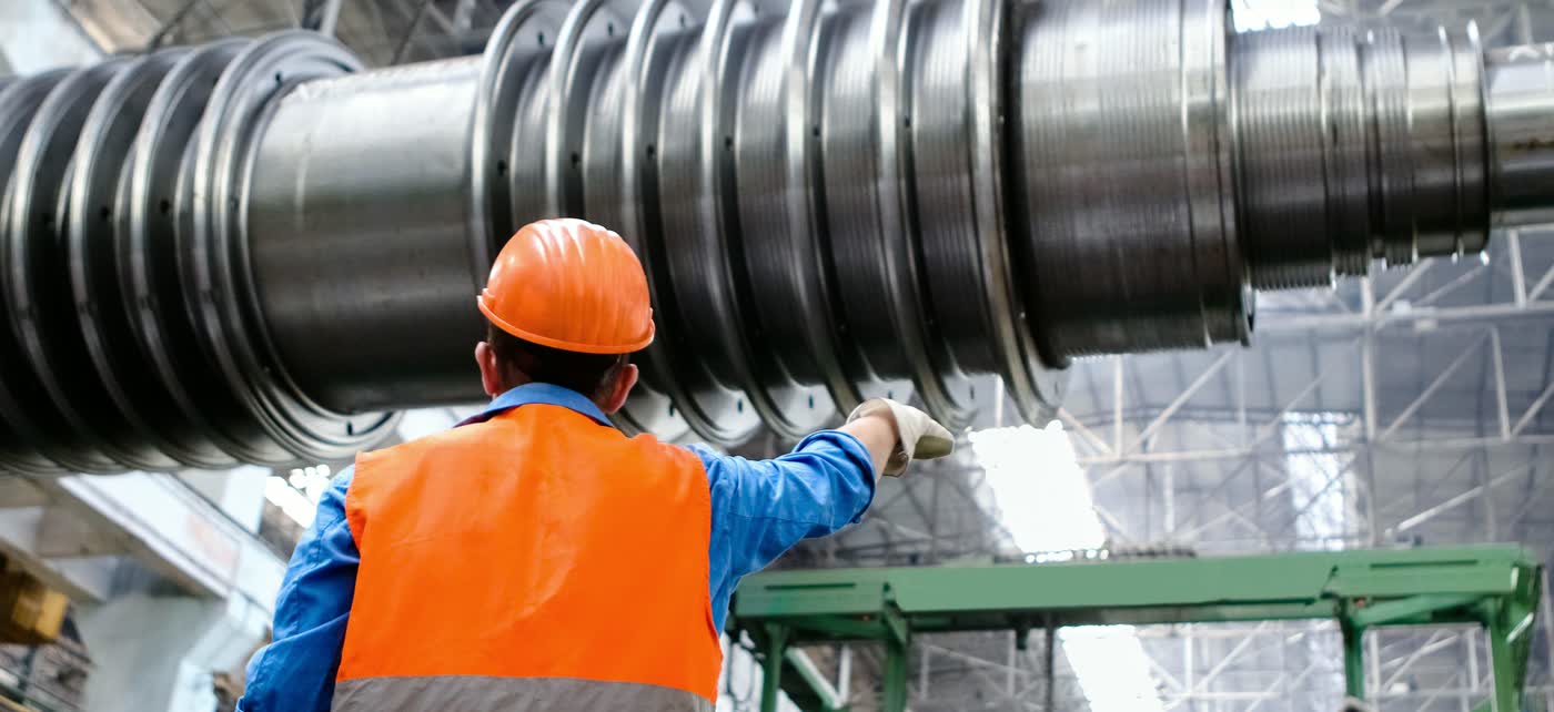 Technician in a high-visibility vest and helmet inspecting a machine in an industrial workshop